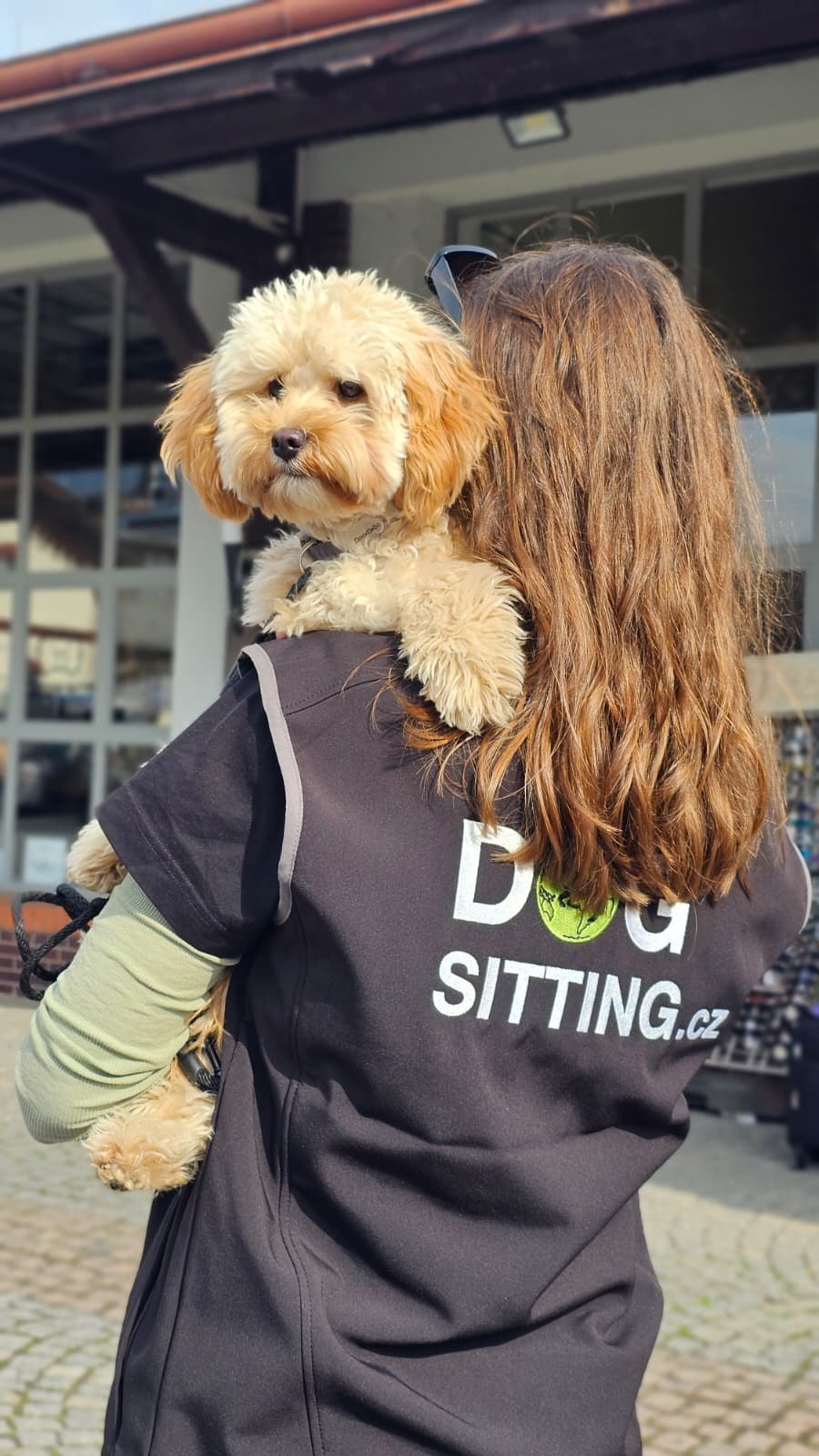 A DOGSITTING.CZ dog-sitter carrying a small dog on her shoulder